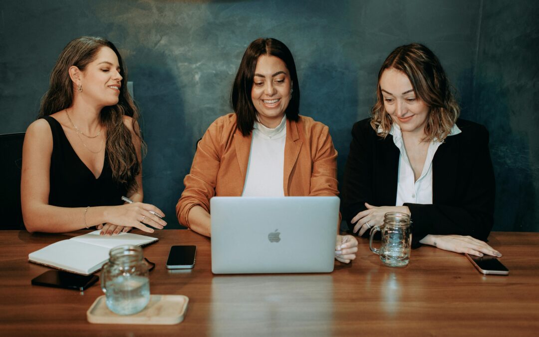 Three women collaborate in front of a laptop.
